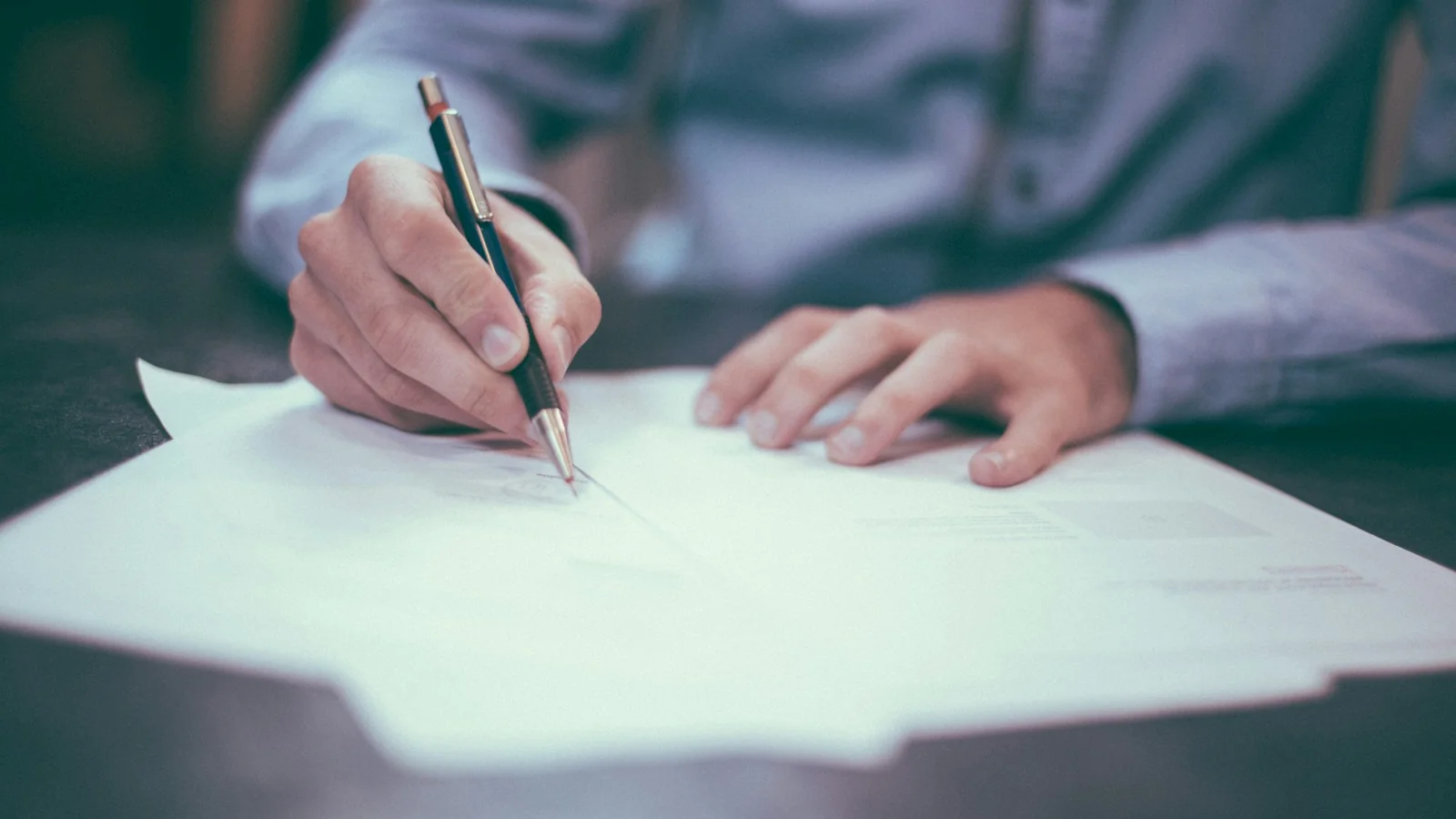 A person signing printed documents with a pen at a desk