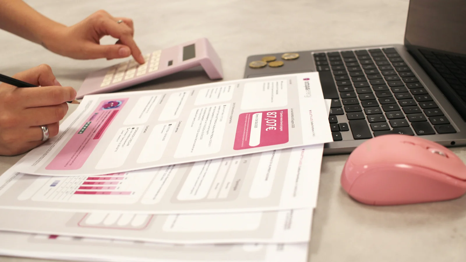 Hands using a calculator over printed invoices next to a laptop