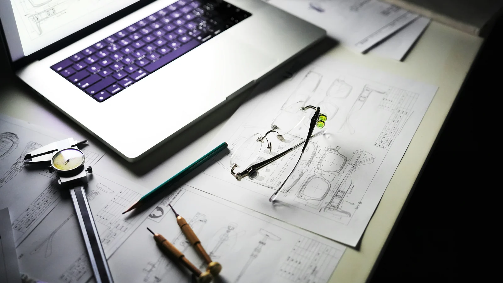 Technical drawings, a laptop and drafting tools on a desk