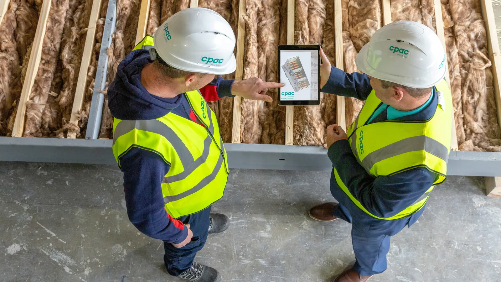 Two people in hard hats and high-visibility vests looking at a tablet on a building site